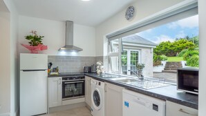 A modern kitchen with a built-in oven, a washing machine, and a large window offering a view of the garden.