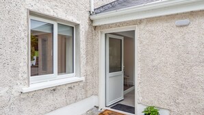 A house with a white exterior, a door, a window, a welcome mat, and a potted plant.