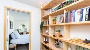 Ein Schlafzimmer mit Bett, Nachttisch und Spiegel. Eine Holzregal mit Büchern und Dekoration.