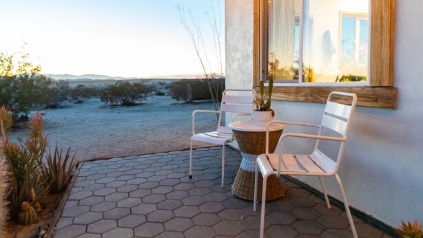 Eine Terrasse im Freien mit sechseckigen Fliesen, zwei weißen Stühlen, einem Korbstuhl-Tisch und einem Blumentopf.