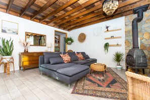 Un salon chaleureux avec un canapé gris foncé, un plafond en bois, un mur en pierre et un poêle à bois noir.