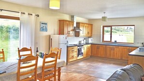 A compact kitchen with wooden cabinets, a refrigerator, a microwave, and a window providing a view of the outdoors.