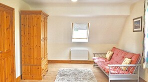 Ein Zimmer mit großem Holzschrank, einem roten Sofa mit Kissen, einem Heizkörper und einem kleinen Fenster.