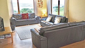 A living room with two grey sofas, a wooden coffee table, and a TV. There is a window with a view of greenery outside.