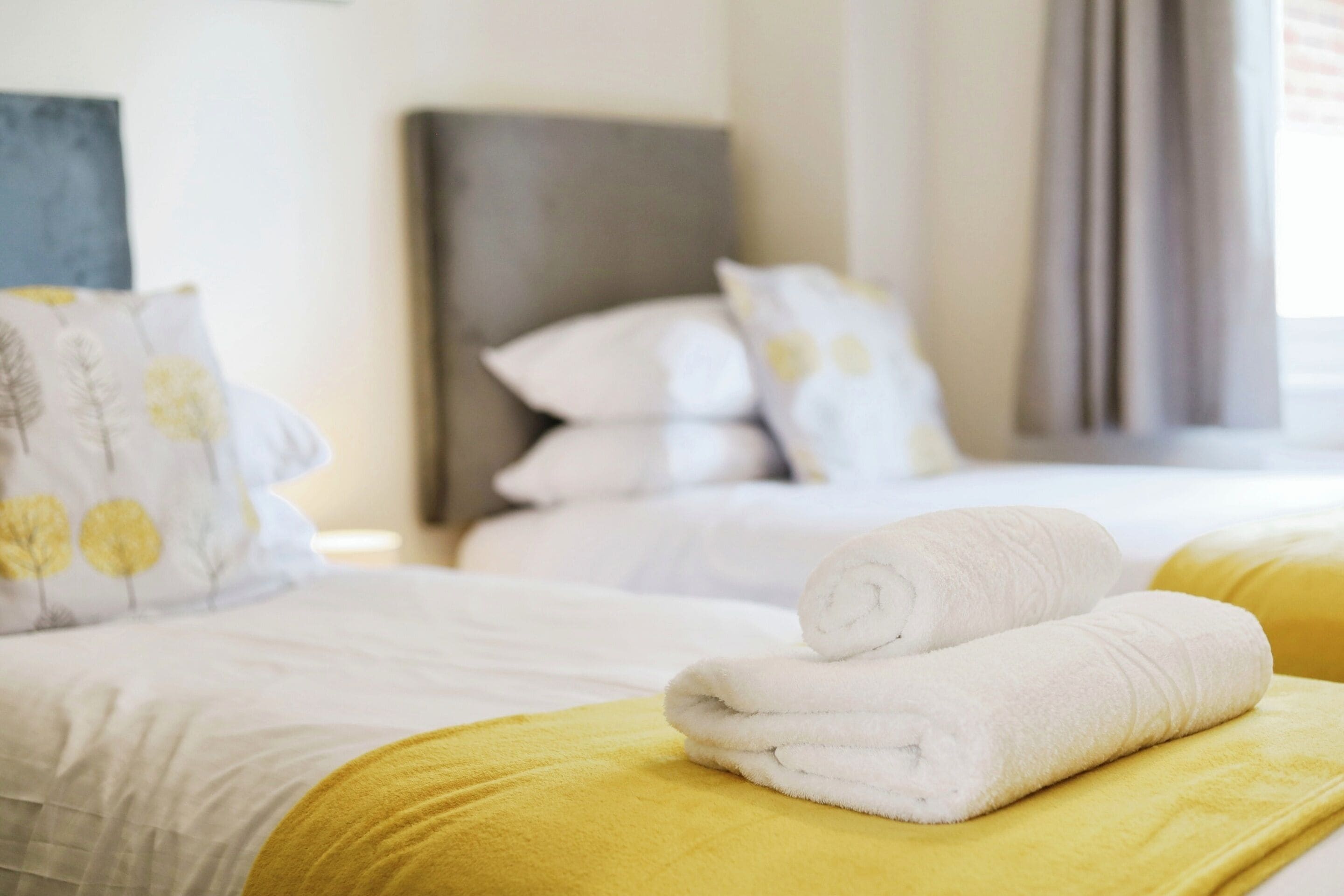 Una camera d'albergo con due letti, ognuno con biancheria bianca e una coperta gialla.