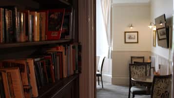 Une pièce avec une bibliothèque remplie de livres, une table à manger avec des chaises et un tableau encadré au mur.