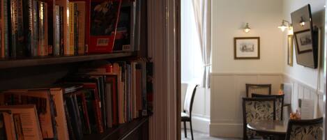 A room with a bookshelf filled with books, a dining table with chairs, and a framed picture on the wall.
