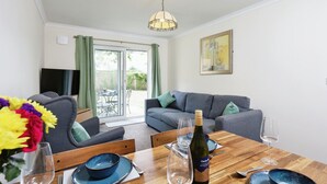 A dining area with a wooden table set for two, a bottle of wine, and a vase of flowers. - The Birdham Hotel & Restaurant (Bembridge)