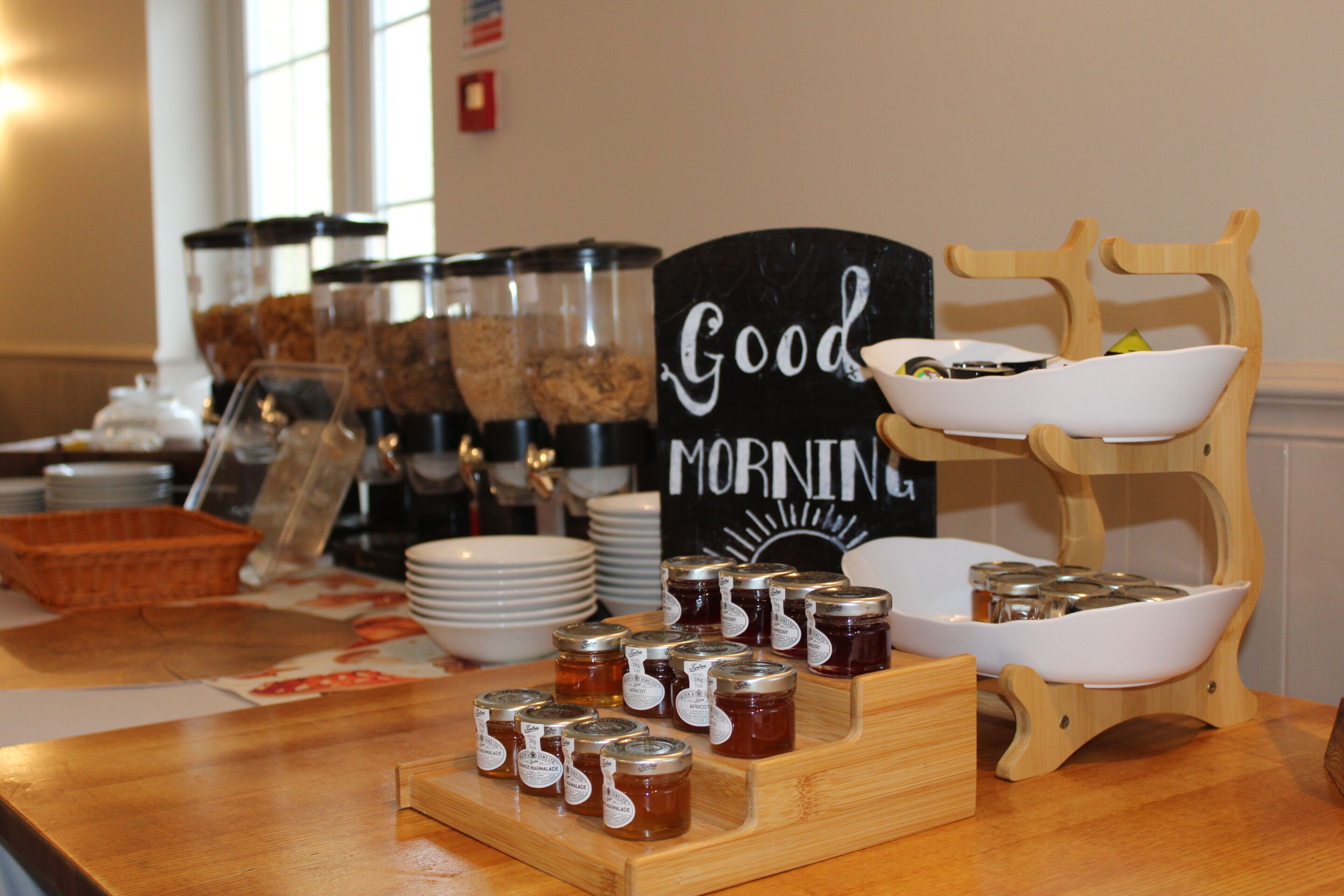 A breakfast buffet with jars of jam, bowls, and a sign that says "Good Morning".