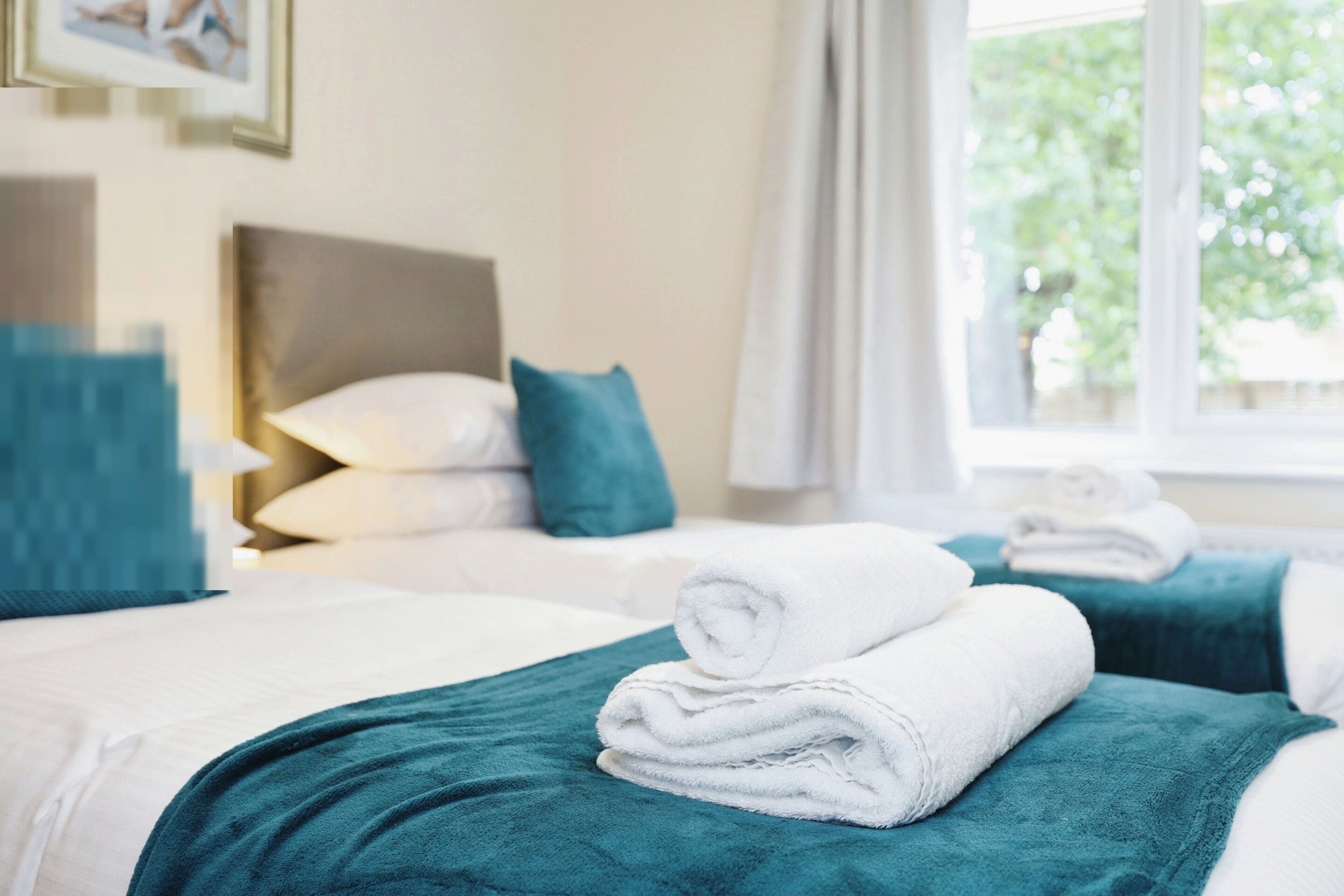 Een hotelkamer met twee bedden, kussenslopen in blauwgroen, witte handdoeken en een raam met uitzicht op groen.