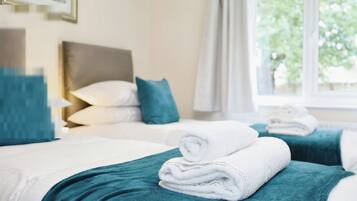Een hotelkamer met twee bedden, kussenslopen in blauwgroen, witte handdoeken en een raam met uitzicht op groen.