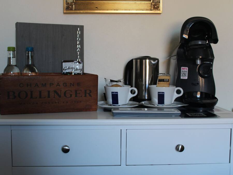 A minibar setup with a bottle of champagne, two cups, a coffee maker, and a kettle.