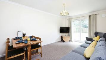 Een woonkamer met een eettafel, stoelen, een bank, een televisie en een raam met gordijnen.