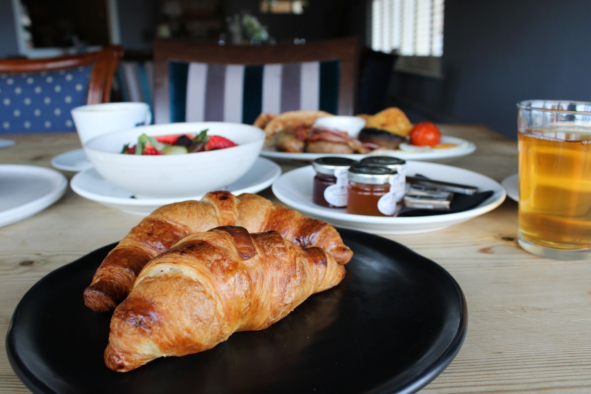 A breakfast setting with croissants, a bowl of fruit, and a glass of tea on a wooden table.
