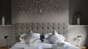 A neatly made bed with a tufted headboard, two decorative pillows, and a set of folded towels.