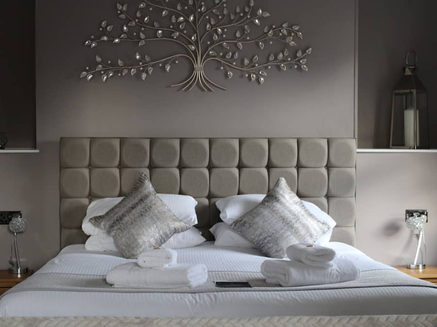 A neatly made bed with a tufted headboard, two decorative pillows, and a set of folded towels.