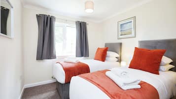 Una habitación de hotel con dos camas, cortinas grises, un cuadro en la pared y una lámpara en el techo.