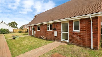 Une maison de plain-pied en briques, avec un toit en tuiles, un porche à l’avant et un petit jardin devant.