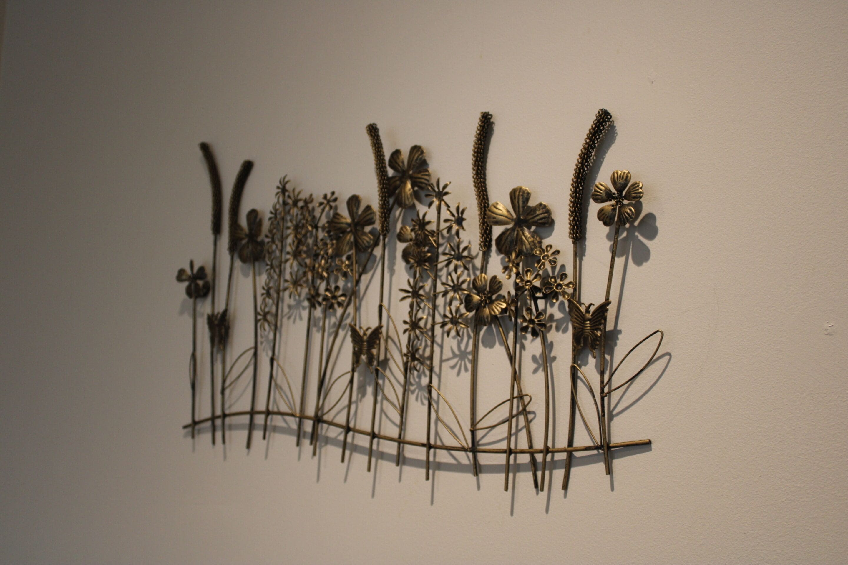 Une sculpture métallique représentant différentes plantes et fleurs, fixée au mur.