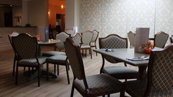 A dining area with wooden chairs and tables, a menu stand, and a patterned wallpaper wall.