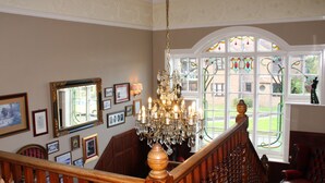 A grand staircase with a wooden handrail and a chandelier, leading to a room with a large arched window and a red carpet. - The Birdham Hotel & Restaurant (Bembridge)