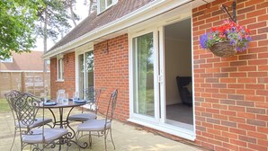 A patio with a table and chairs, a hanging flower basket, and a sliding glass door leading to an interior space. - The Birdham Hotel & Restaurant (Bembridge)