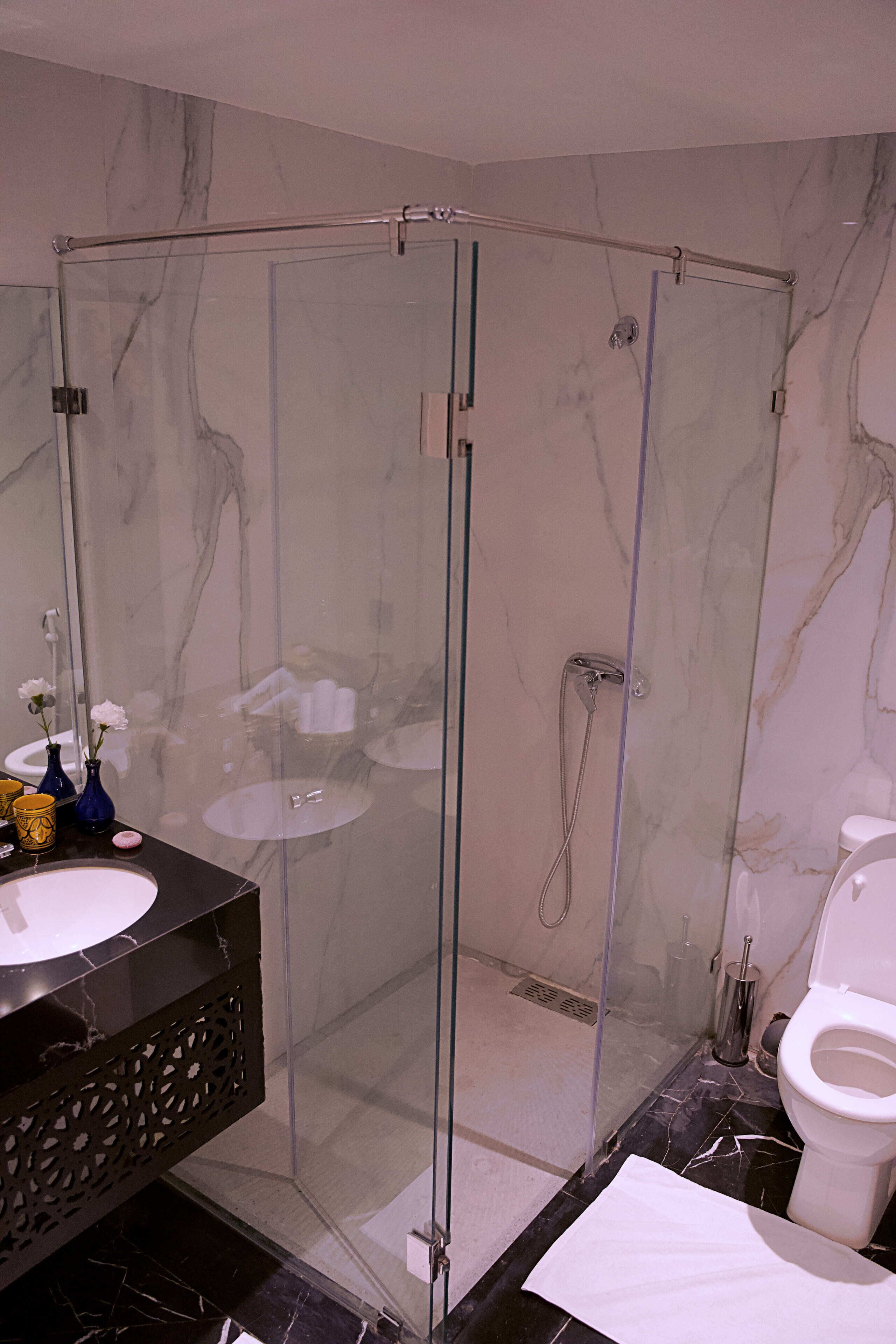 A modern bathroom with a glass-enclosed shower, a marble sink, and a toilet.