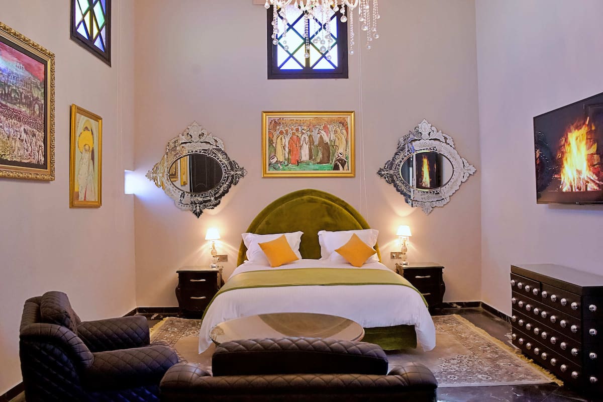 A hotel room with a large bed, two nightstands, a chandelier, and artwork on the walls.