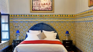 A bedroom with a large bed, a chandelier, patterned walls, and a framed picture on the wall. - Riad Dar Chrifa (Rabat)
