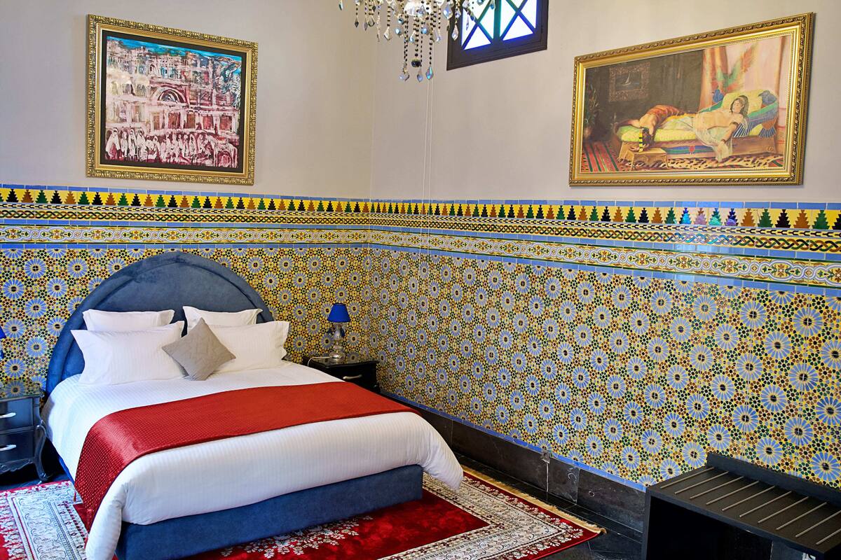 A bedroom with a large bed, a nightstand, a chandelier, and patterned walls.