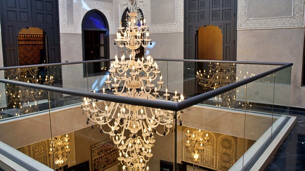A grand chandelier in a spacious lobby with high ceilings and ornate wall decorations. - Riad Dar Chrifa (Rabat)