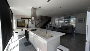 Una cuina moderna amb una illa central, una zona de menjador amb sofà i una escala que condueix a un altre nivell.