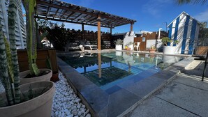 Una piscina amb una pèrgola, plantes en testos i un pont de fusta.