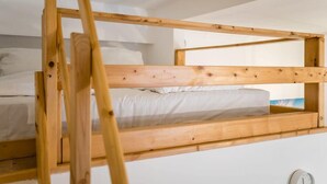 Ein Stockbett mit Holzbettgestell, weißer Bettwäsche und einem kleinen Fenster.