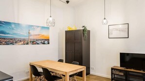 Ein modernes Wohnzimmer mit einem Holzespeisetisch, schwarzen Stühlen, einer dunklen Kommode, einem Fernseher auf einem schwarzen Schrank und zwei Pendelleuchten.