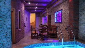 A swimming pool area with a stone wall, wooden furniture, and a staircase leading to another room. - Aleppo Hotel in Yerevan (Yerevan)