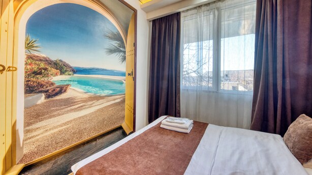 A hotel room with a bed, a window with curtains, and a mural of a beach scene. - Aleppo Hotel in Yerevan (Yerevan)
