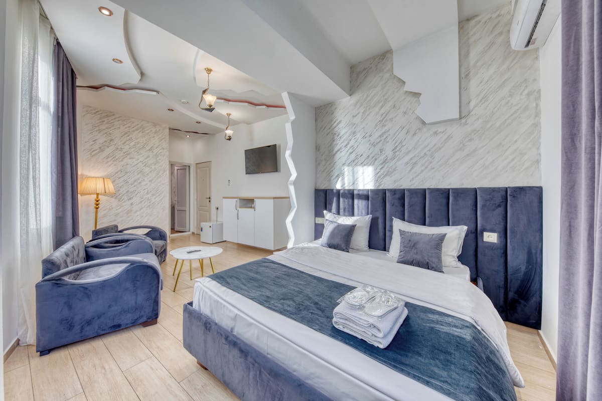 A modern hotel room with a large bed, a seating area with sofas, a small round table, and a marble-patterned wall.