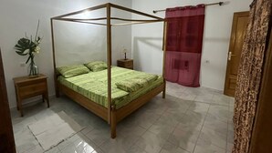 Un dormitori amb un llit amb cortines, una tauleta de nit, una taula petita, un ram de flors i una cortina vermella.