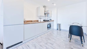 Une cuisine moderne avec des meubles blancs, un plan de travail en bois et un coin repas agrémenté d’une chaise noire.