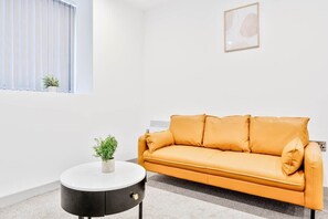 A modern living room with a sofa, a round table with a plant, and a window with blinds. - Smart 1 Bed Apartment in Wolverhampton (Wolverhampton)
