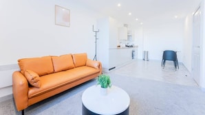 Un salon moderne avec un canapé en cuir, une table basse ronde agrémentée d’une plante, et un coin cuisine à l’arrière-plan.