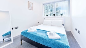 Une chambre d’hôtel avec un grand lit, une fenêtre donnant sur des arbres, un miroir et une petite table.