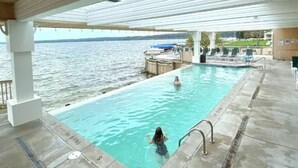 Ein Poolbereich mit Blick auf das Wasser, einer überdachten Terrasse und Liegestühlen.