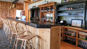 Eine Bar mit Holzsesseln, einer Theke und Regalen voller Flaschen und Gläsern.