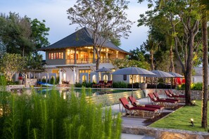 Una casa grande con piscina, sillas de descanso y sombrillas.