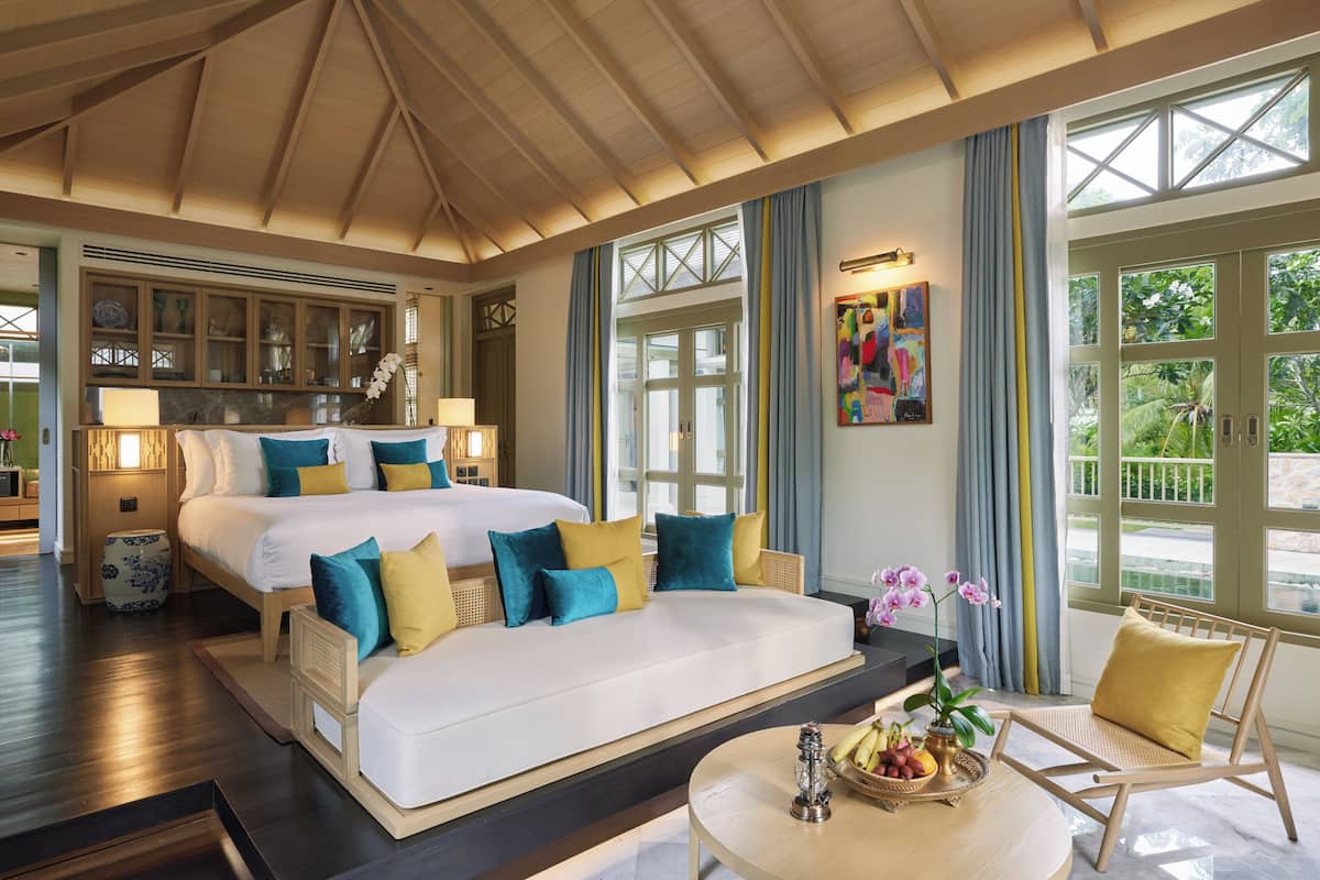 Ein Hotelzimmer mit einem großen Bett, einer Sitzecke, einem Esstisch mit Früchten und Blick auf Grünflächen.