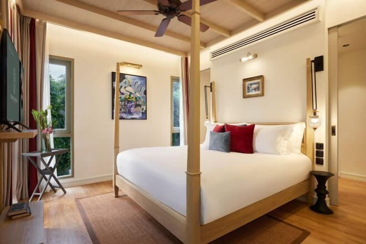 Ein Himmelbett mit Deckenventilator, ein Gemälde an der Wand und ein Fenster mit Vorhängen.