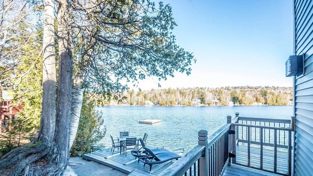 A wooden deck with a view of a lake, a dock, and a boat.