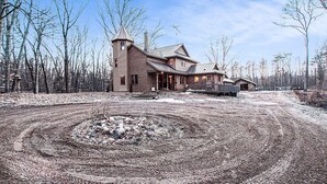 A rustic log cabin with a prominent tower, surrounded by a forested area and a gravel driveway. - Private 40-Acre Retreat | Hot Tub, Trails, Games & Fire Pit (Hopkins)